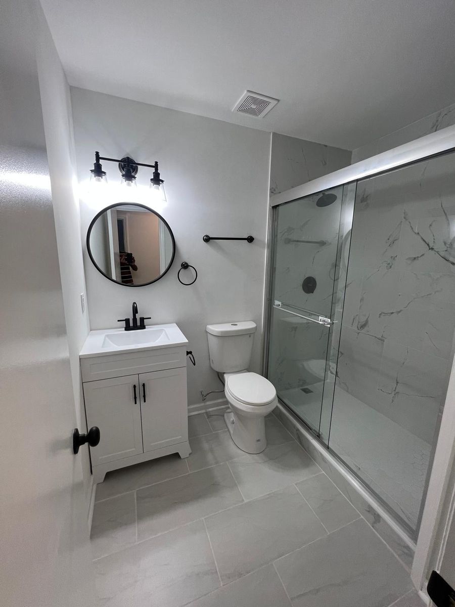 A second renovated bathroom with a glass-enclosed marble-look tile shower, white vanity, and black fixtures