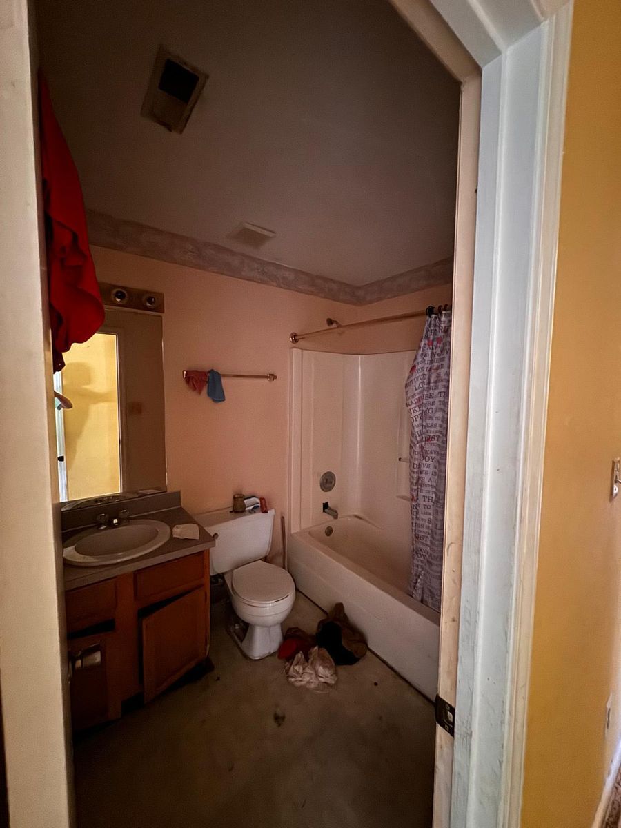 A bathroom before renovation: dated vanity, stained walls, and a bare floor