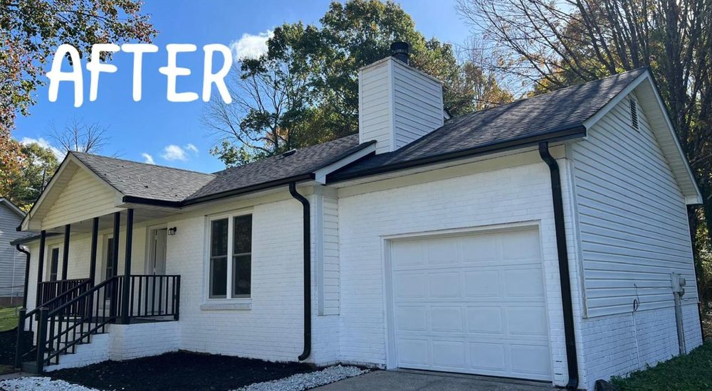 The same house after renovation: painted white brick, new dark roof and gutters, and black porch railings