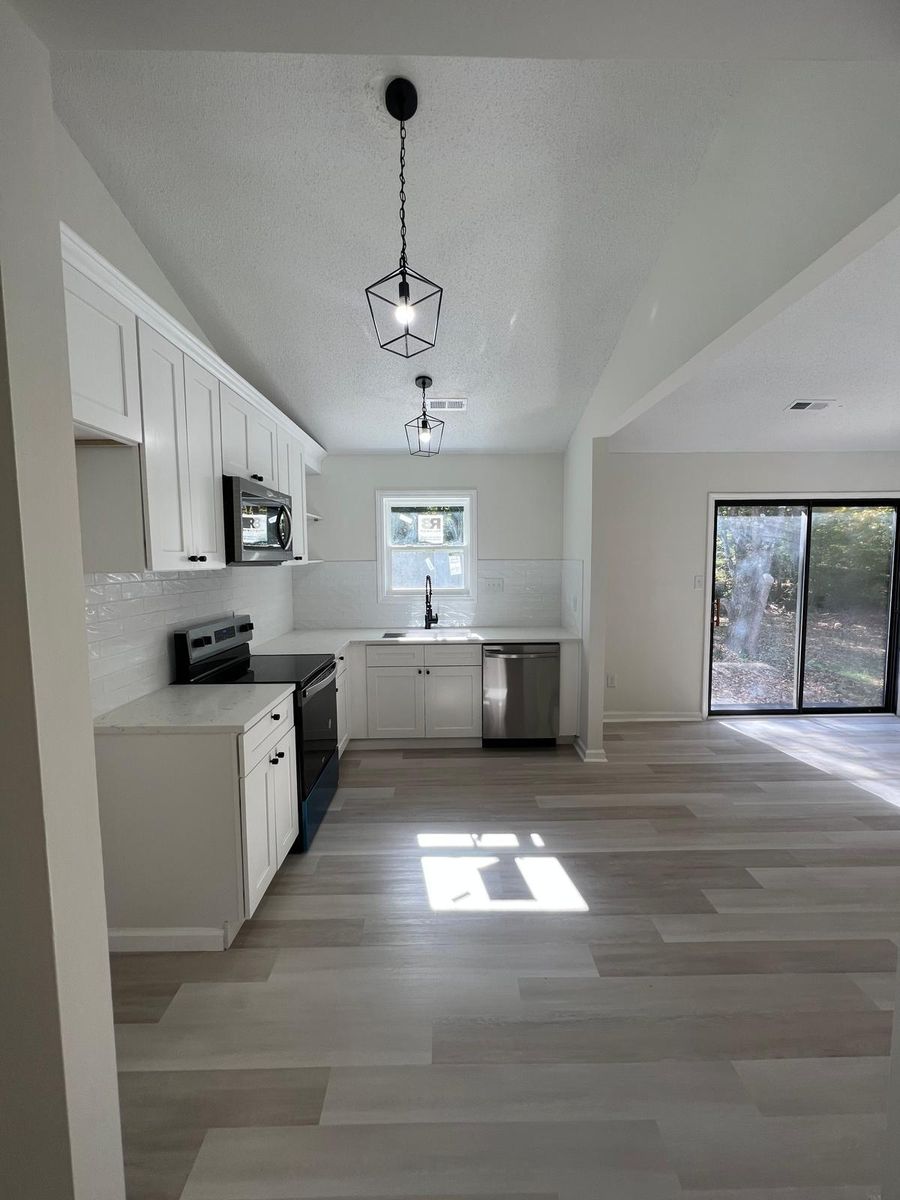 The kitchen after renovation: white shaker cabinets, subway tile backsplash, stainless appliances, pendant lights, and new plank flooring