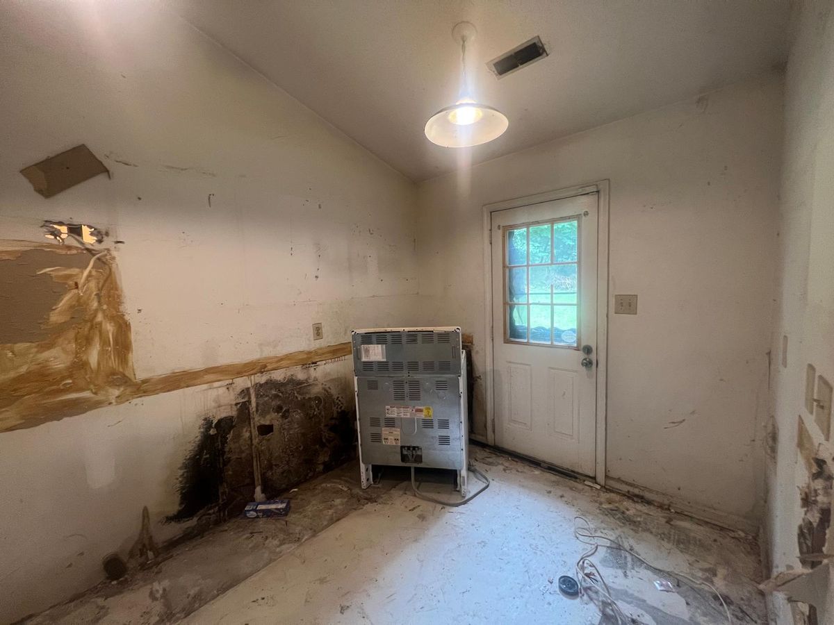 The kitchen before renovation: water-damaged walls, no cabinets, and a bare subfloor